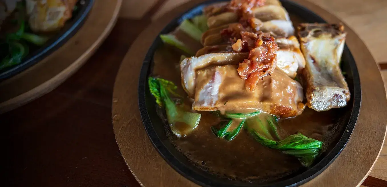 Dry Aged Duroc Pork Rib Eye on a sizzling plate with baby bok choy and guava bacon jam at Kona Inn Restaurant